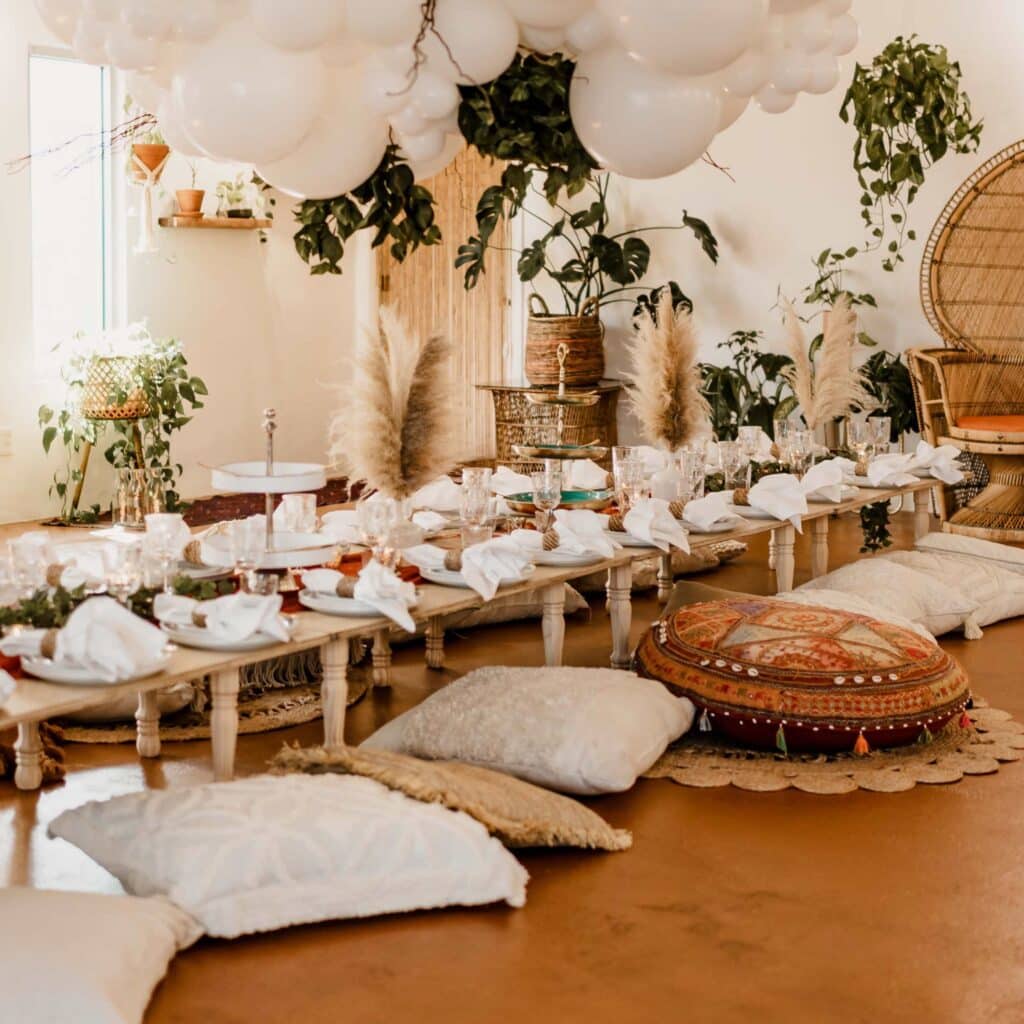 Boho Greenery And Floral Party Indoor with long wooden table setups, pillows and greenery garland